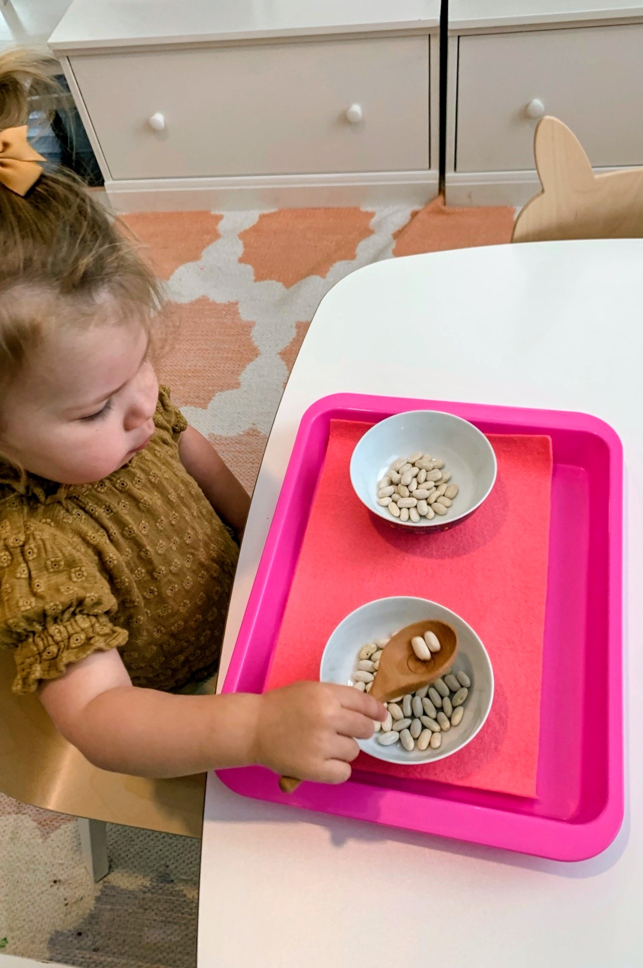 Child sorting beans with a wooden spoon on a Montessori tray