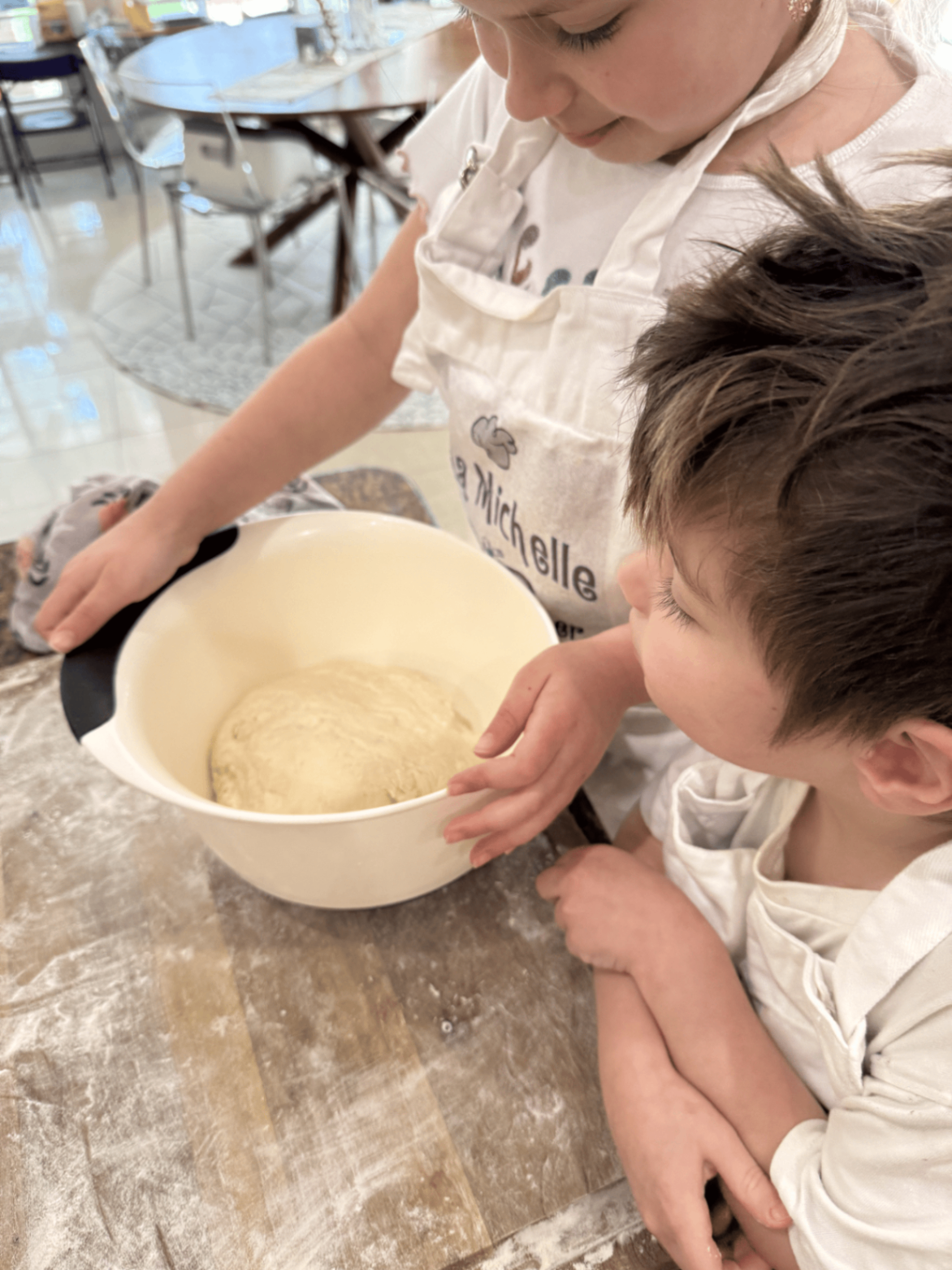 Two children checking rising dough in a mixing bowl during a baking activity