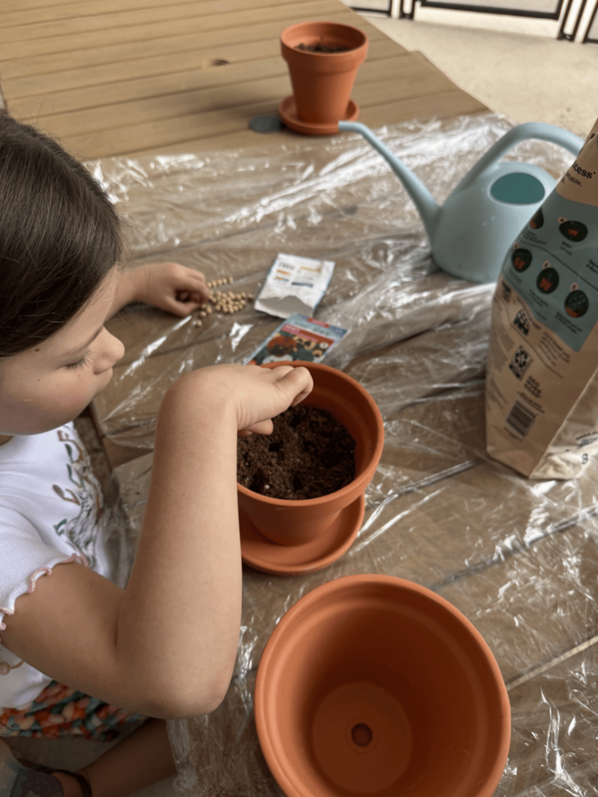Child placing seeds into soil in a terracotta pot